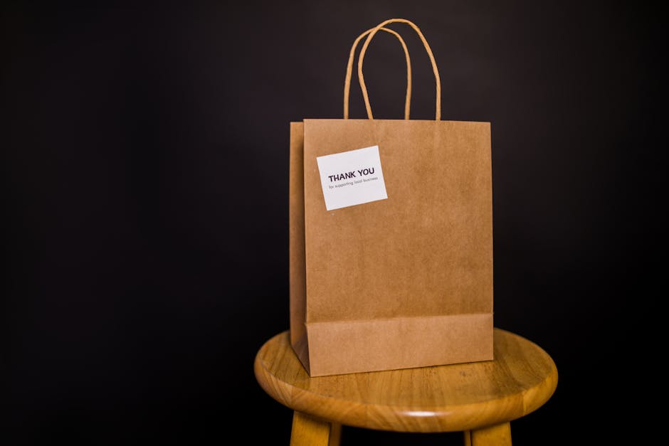 Brown paper bag with thank you note placed on a wooden stool against a black background.